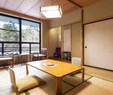 Tatami room with low wooden table, floor chairs, shoji doors and window overlooking wooded hillside