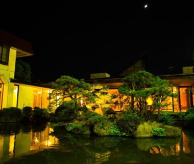 Illuminated courtyard garden with pond reflecting Hotel Sekitei buildings at night in Yamanashi