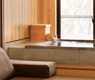 Tatami room with cushioned seating and stone in-room soaking tub by window overlooking trees