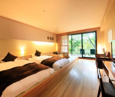 Spacious room with low beds on wooden platform and sliding glass doors opening to a garden balcony at Hotel Shikisai,
