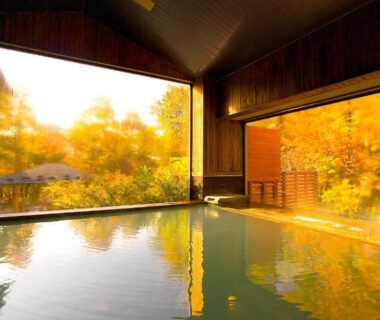 Indoor onsen bath with wooden interior overlooking golden foliage at Hotel Shikisai in Tochigi