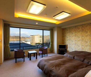 Twin beds with seating by large window overlooking town and distant hills at Hotel Shion in Iwate