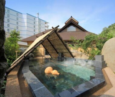 Stone onsen bath with thatched shelter and hotel building backdrop at Hotel Shion, Iwate, Tōhoku