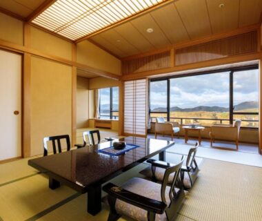 Traditional tatami room with low dining table, zaisu chairs and large window overlooking distant hills at Hotel Shion, Iwate
