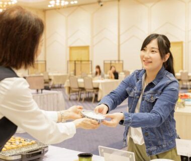Smiling guest receives a plate from staff at a buffet table in Hotel Shion dining hall, Iwate, Tōhoku