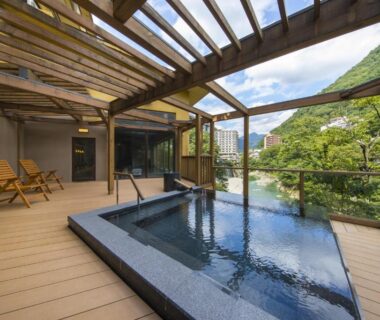 Rectangular outdoor onsen bath on wooden deck under pergola with chairs and mountain view at Hotel Shirakawa Yunokura Tochigi