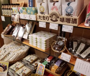 Assorted packaged snacks and condiments on wooden shelves at Hotel Shirakawa Yunokura souvenir shop, Tochigi