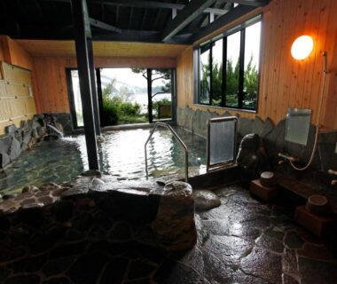 Indoor stone onsen with wooden walls and shower stations at Hotel Shosenkaku Romankan Kumamoto Kyushu