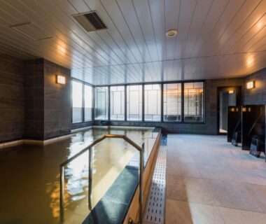 Spacious indoor onsen bath with tiled pool, handrail and shower stalls at Hotel Sonia Otaru Hokkaido