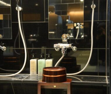 Dark tiled shower area with wooden stool and toiletries at Hotel Sugicho bathroom