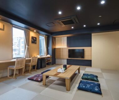 Spacious tatami room with low table, floor cushions, window desks and television at Hotel Sugicho in Kyoto