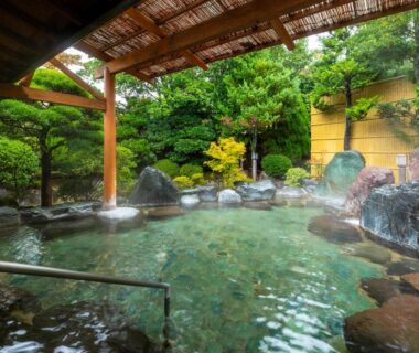 Steaming rock-lined outdoor onsen pool with wooden roof and garden at Hotel Sunvalley Izunagaoka Shizuoka