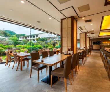 Spacious dining room with wooden tables and chairs opening onto a manicured garden at Hotel Sunvalley Izunagaoka, Shizuoka