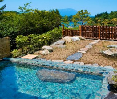 Outdoor stone onsen pool with landscaped garden and distant hills at Hotel Taikan, Iwate