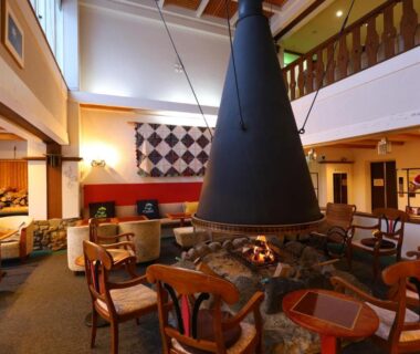 Spacious two-story lobby with central stone hearth, seating area and traditional Japanese accents at Hotel Takimoto, Nagano