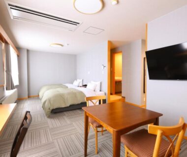Bright modern guest room with twin beds, table and wall television at Hotel Takimoto in Nagano Chūbu