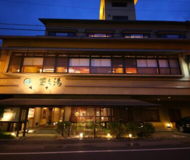 Lit multi-story ryokan facade at dusk with warm windows and entrance, Hotel Tamanoyu in Nagano
