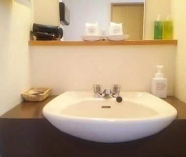 White sink and mirror with soap dispenser and toiletries on a wooden counter in Hotel Tetora bathroom, Tsuruoka, Yamagata