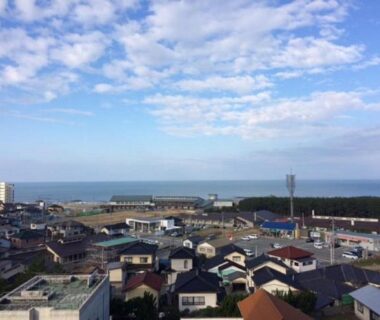 Aerial view of seaside town rooftops with distant coastline and blue sky near Hotel Tetora in Yamagata