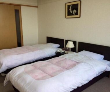 Twin beds with bedside lamp, sliding door and framed art in Hotel Tetora Resort Tsuruoka, Yamagata