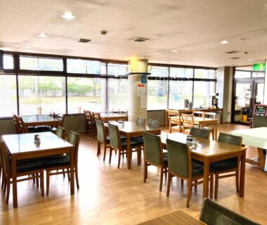 Spacious ryokan dining hall with wooden tables and chairs facing large windows at Hotel Tetora Yunokawaonsen Hokkaidō