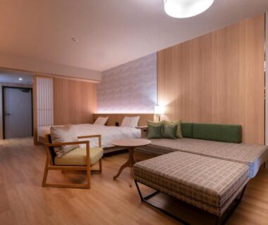 Wooden interior room with two beds, lounge chair, shoji screens and cushioned bench at Hotel Tokinoza in Mie, Japan