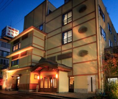 Evening exterior of Hotel Tsubakino with warm lit entrance and windows under a deep blue sky