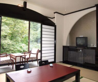 Traditional tatami room with low table, shoji screens and chairs overlooking wooded garden at Hotel Uguisu in Iwate
