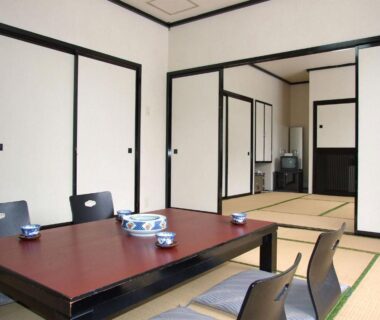 Tatami room with low table, zaisu floor chairs, fusuma sliding doors and small TV at Hotel Uguisu in Iwate