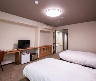 Two single beds, desk, TV, and compact fridge in a simple hotel-style room at Hotel Umenoyu, Nagano