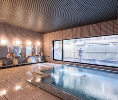 Tiled indoor onsen with washing stations and large window at Hotel Umenoyu, Nagano, Chūbu