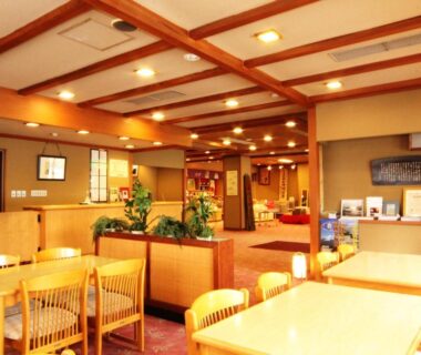 Warm communal dining space with wooden tables, chairs, ceiling beams and potted plants at Hotel Uzuraya in Nagano