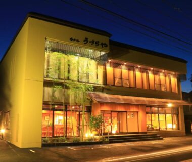 Warmly lit two-story ryokan exterior at dusk with illuminated windows and entrance, Hotel Uzuraya, Nagano