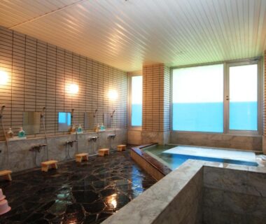 Indoor bathing area with soaking tubs, wash stations, tiled walls and large windows at Hotel Wakatsuki Nagano