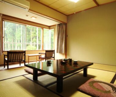 Traditional tatami room with low dining table, floor cushions and window seating overlooking greenery at Hotel Wakatsuki in Nagano