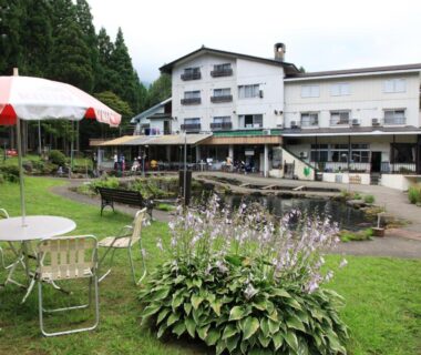 Outdoor lawn seating with umbrellas in front of Hotel Wakatsuki surrounded by forested hills in Nagano Chūbu