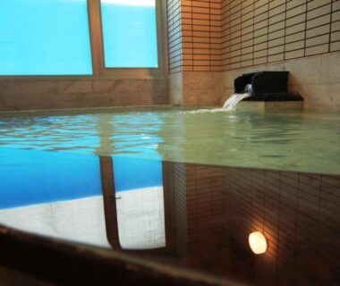 Indoor onsen bath with water spout and tiled walls, frosted window view at Hotel Wakatsuki Nagano