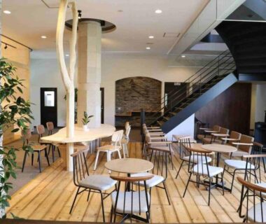 Bright communal lounge with wooden floors, round tables and staircase at Hotel Yume-no-yu, Nagano, Chūbu Japan