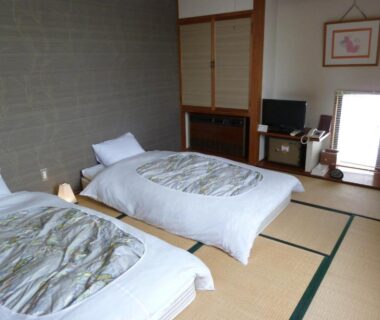 Tatami floor room with two low beds, sliding shoji screens, TV and small cabinet at Hotel Yume-no-yu, Nagano