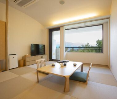 Tatami room with low wooden table, floor cushions, TV and large window overlooking greenery at Hotel Yumeshizuku Kumamoto