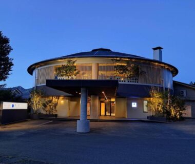 Round two-storey ryokan building with illuminated entrance and curved upper balcony at dusk in Kumamoto