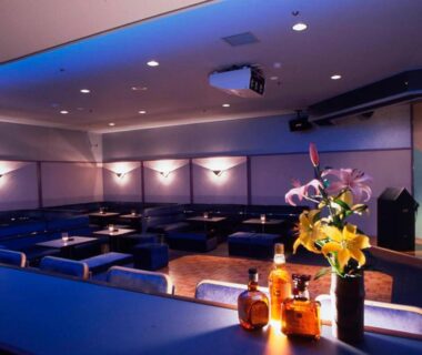 Dim hotel lounge counter with bottles, flowers, booth seating and projector stage at Hotel Yumoto in Niigata