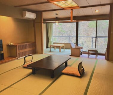 Spacious tatami room with low table, zabuton cushions and balcony seating at Hotel Yunishigawa in Tochigi