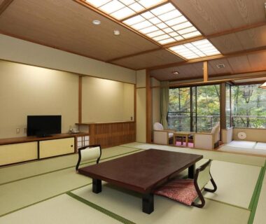 Traditional tatami room with low table, floor cushions, wooden cabinetry and garden-facing sliding windows at a Tochigi ryokan