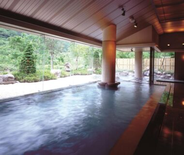 Spacious indoor onsen with large glass wall overlooking lush garden at Hotel Yunojin in Gunma