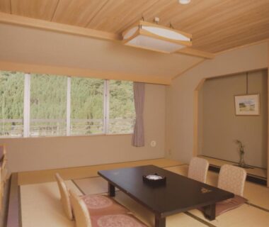 Traditional tatami room with low table, zaisu chairs and green hillside view at Hotel Yunojin, Gunma