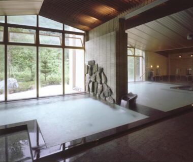 Indoor onsen with stone feature, wooden ceiling and large windows at Hotel Yunojin, Gunma, Japan