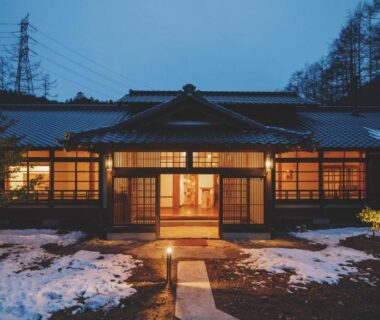Warmly lit traditional ryokan entrance at dusk with snow patches and shoji-style windows, Hotorinite Yamanashi