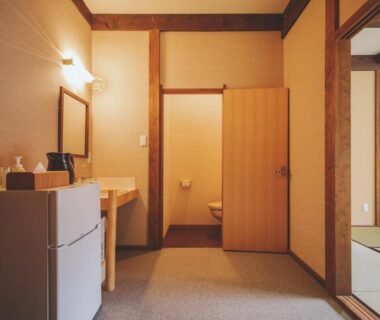 Interior with tatami room, low table, wooden sink, small refrigerator and open restroom door at Hotorinite, Yamanashi