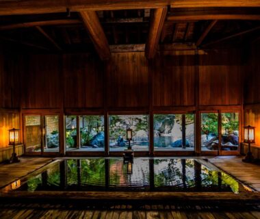 Spacious indoor wooden onsen hall with reflecting pool, warm lantern lighting and garden view at a Gunma ryokan